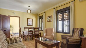 Una sala de estar con sofá, sillón, mesa de comedor, sillas y una ventana con cortinas.