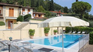 Ein Swimmingpool mit Liegestühlen, einer überdachten Liegefläche und einem Gebäude mit Treppe und Kübelpflanzen.