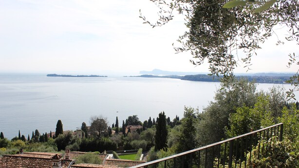 Eine Terrasse mit Blick auf ein großes Gewässer, umgeben von Grünflächen und Gebäuden mit Terrakotta-Dächern.