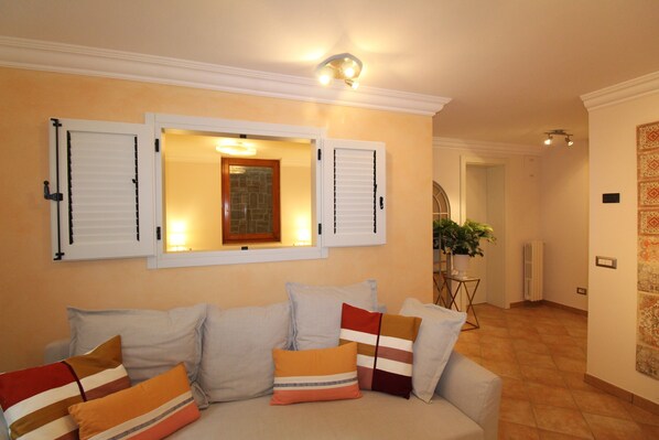 A living room with a sofa, pillows, a window with shutters, a potted plant, and a radiator.