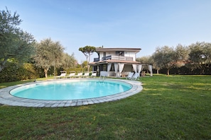 A two-story house with a swimming pool, surrounded by a lawn and trees.
