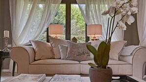 Una sala de estar con un sofá color beige, una planta en maceta y dos lámparas.