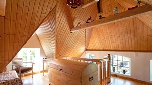 A high-ceilinged room with wooden beams, a wooden chest, a chair, and a table.