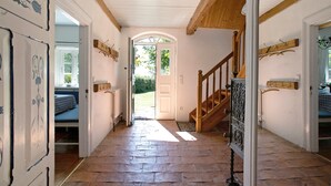A hallway with a wooden staircase, a door leading outside, and a bench with a checkered tablecloth.