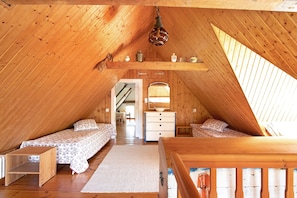 A cozy attic bedroom with two beds, a wooden ceiling, a dresser, and a window.