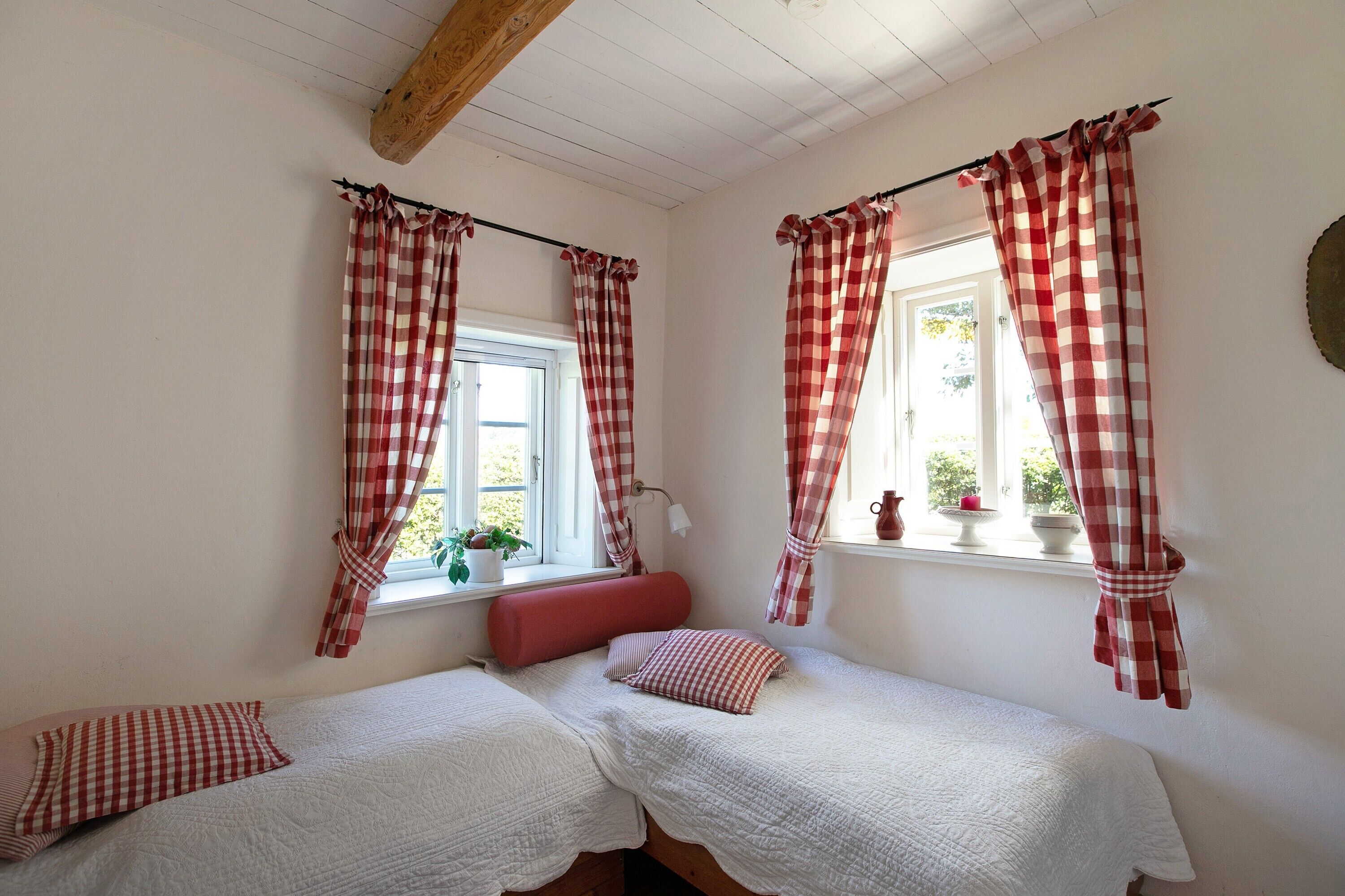 Ein Zimmer mit zwei Einzelbetten, karierten Vorhängen, einem Fenster mit Blick und einem kleinen Tisch mit einer Pflanze.