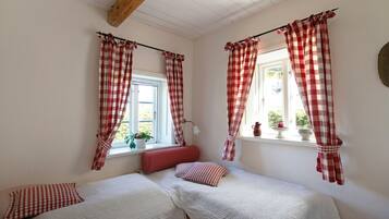 Ein Zimmer mit zwei Einzelbetten, karierten Vorhängen, einem Fenster mit Blick und einem kleinen Tisch mit einer Pflanze.