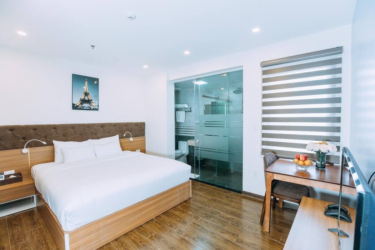 Et moderne hotelværelse med en stor seng, et skrivebord med telefon og et bruseområde med glasvægge.