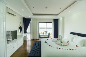 A hotel room with a bed, a TV, a balcony with a table and chairs, and a view of the water.