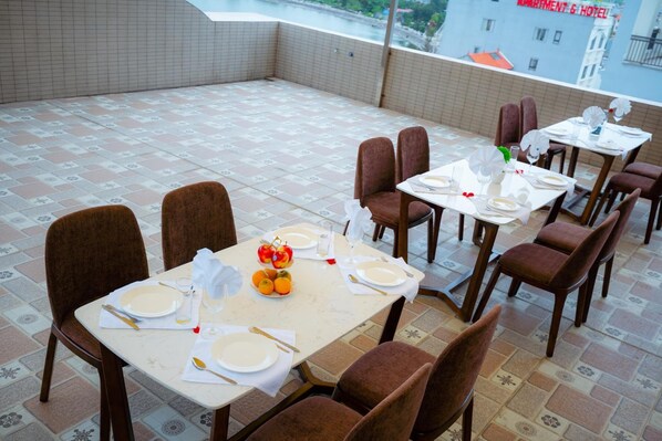 A rooftop dining area with multiple tables set for dining, chairs, and a view of buildings in the background. - Queenie Hotel (Hai Phong)