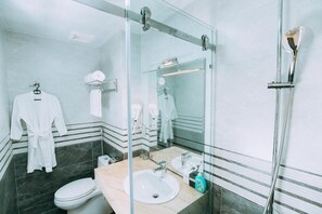 A modern bathroom with a glass shower enclosure, a marble-tiled vanity, a white sink, and a large mirror. - Queenie Hotel (Hai Phong)