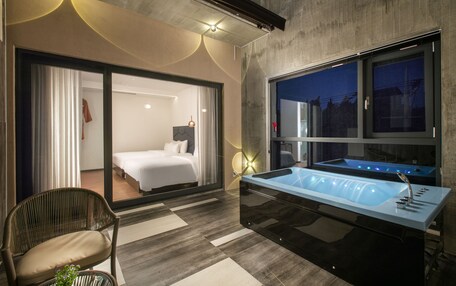 A modern hotel room with a large bathtub, a bed, and a seating area.