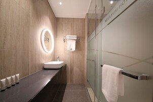 Un baño moderno con cabina de ducha de vidrio, tocador con lavamanos y perchero.