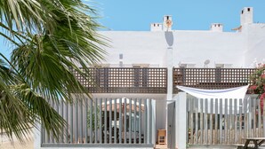 A modern building with a white facade, a wooden fence, and a palm tree in the foreground.