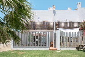 A modern building with a white facade, a wooden fence, and a palm tree in the foreground.