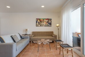 Un salon avec un canapé, une table basse et des fauteuils, un tableau au mur et une fenêtre avec des rideaux.
