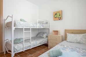 Un lit superposé avec un lit inférieur, une table de chevet en bois, un lit simple avec une tête de lit et un tableau représentant un scooter, accroché au mur.