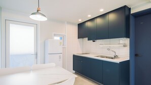 A modern kitchen with dark blue cabinets, a white countertop, and a built-in oven. - Unicorn Pension (Seogwipo)