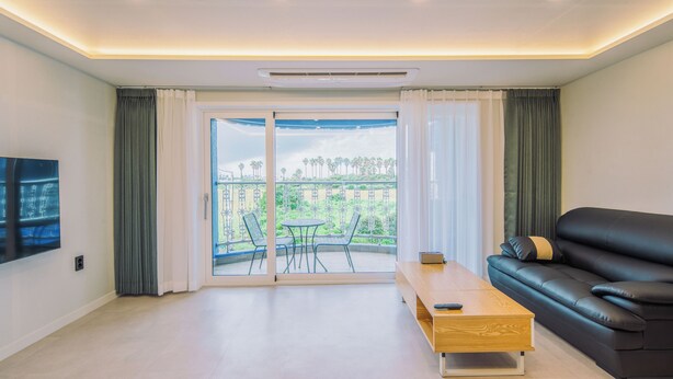 A modern living room with a black leather sofa, a wooden coffee table, and a TV mounted on the wall. - Unicorn Pension (Seogwipo)