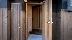 A narrow wooden entrance with a sliding door leading to a room with a dark wooden floor and a vertical wooden panel wall. - Casa Grapp Tengachaya II (Osaka)