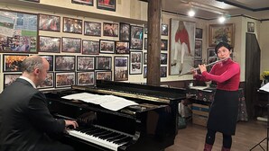 Een kamer met een vleugel, een fluitspeler en een pianist.