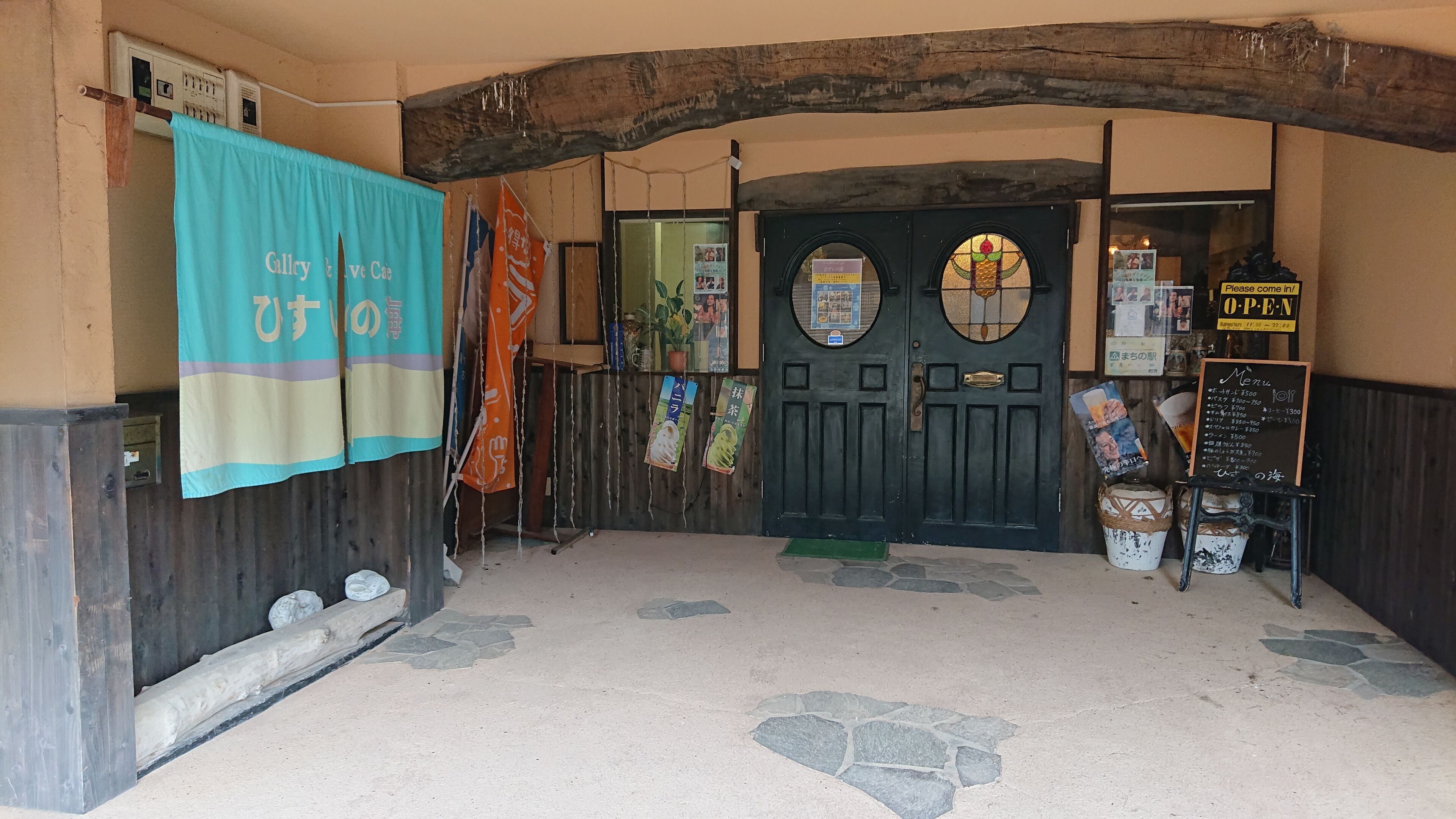 Una entrada rústica con un arco de madera, una puerta negra con un ventanal circular y un cartel con el menú.