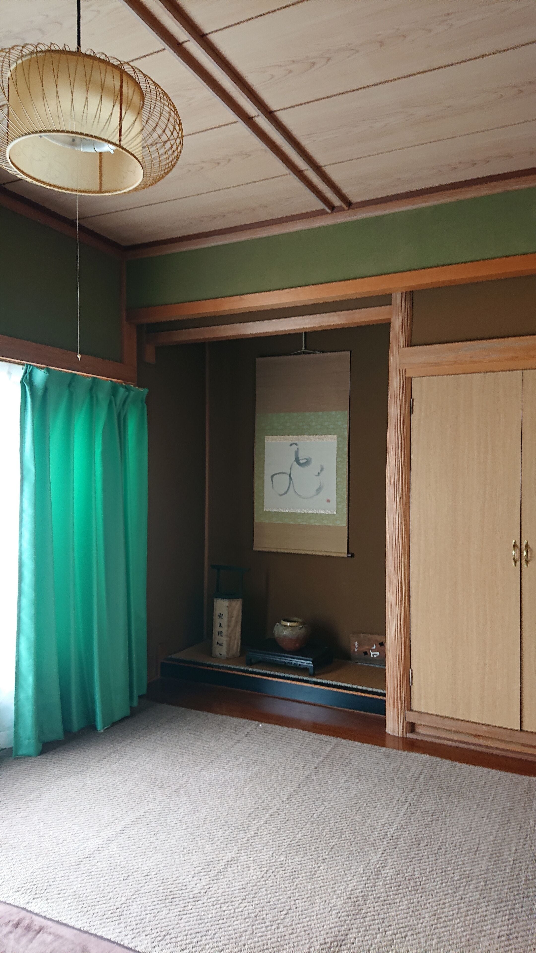 A room with a wooden cabinet, a hanging lamp, a green curtain, and a framed picture on the wall.