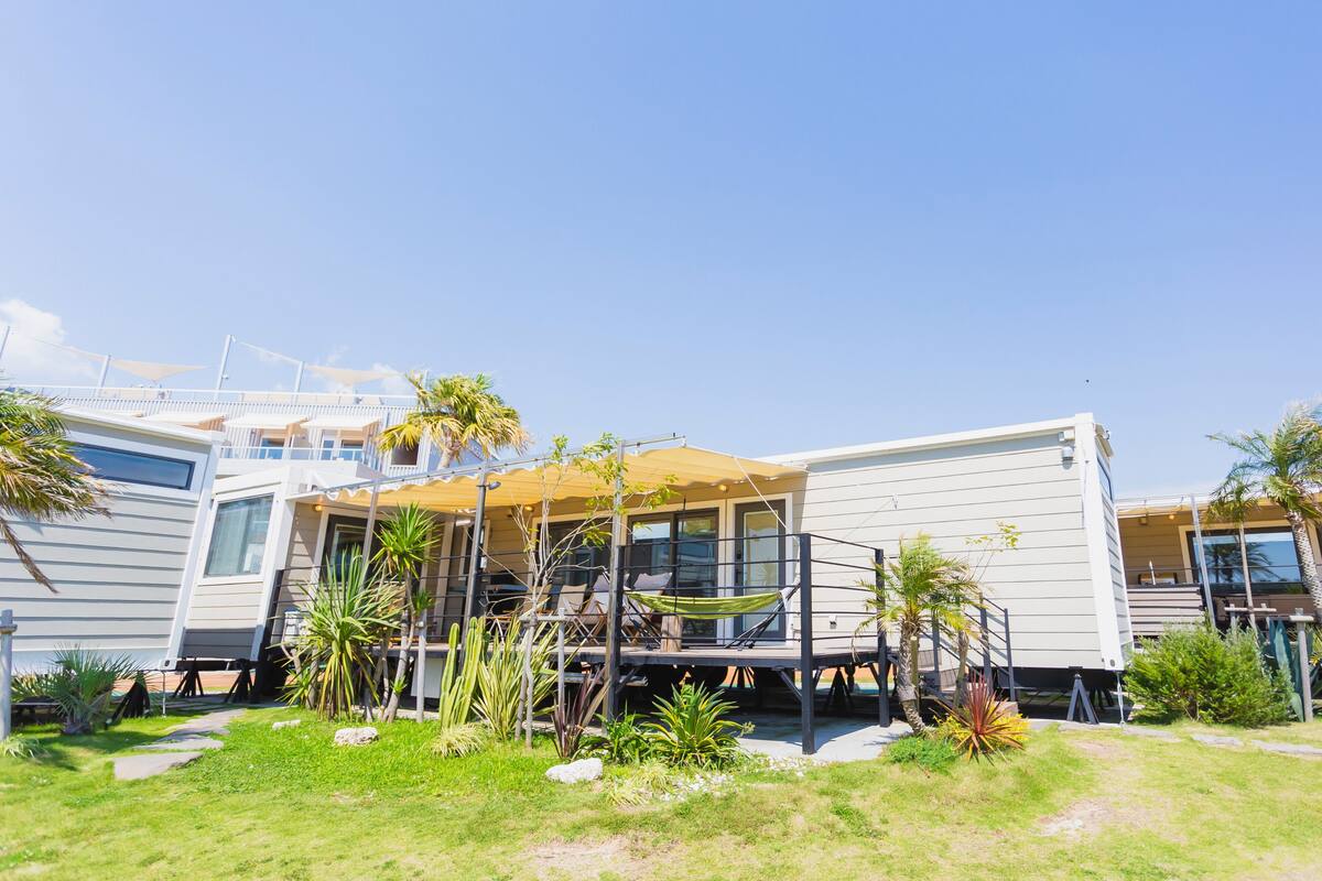 Un bâtiment moderne à plusieurs étages, doté d’un toit plat, de grandes fenêtres et d’un espace extérieur couvert aménagé avec des sièges.