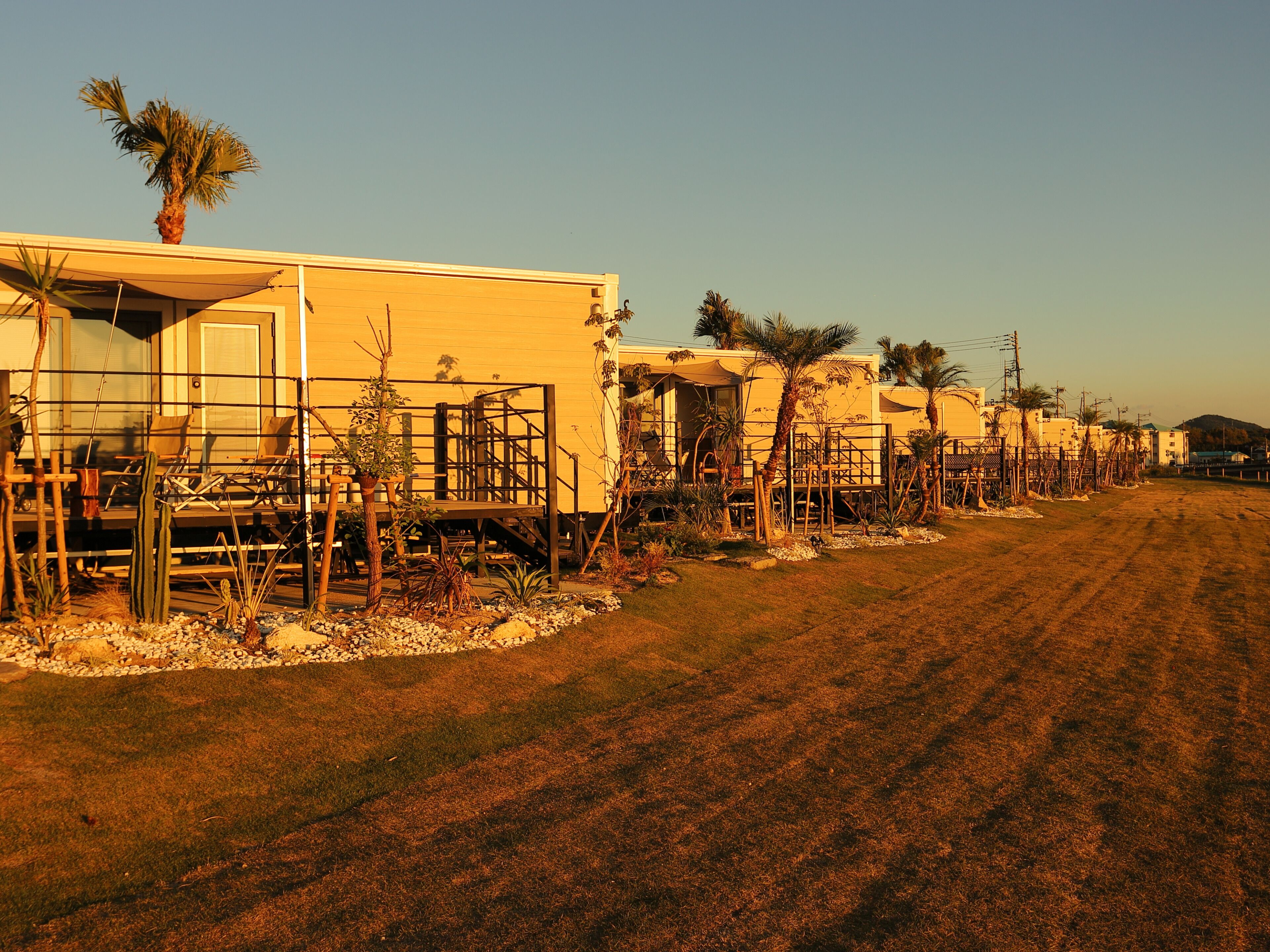 A row of single-story buildings with a flat roof, surrounded by a gravel driveway and sparse vegetation.
