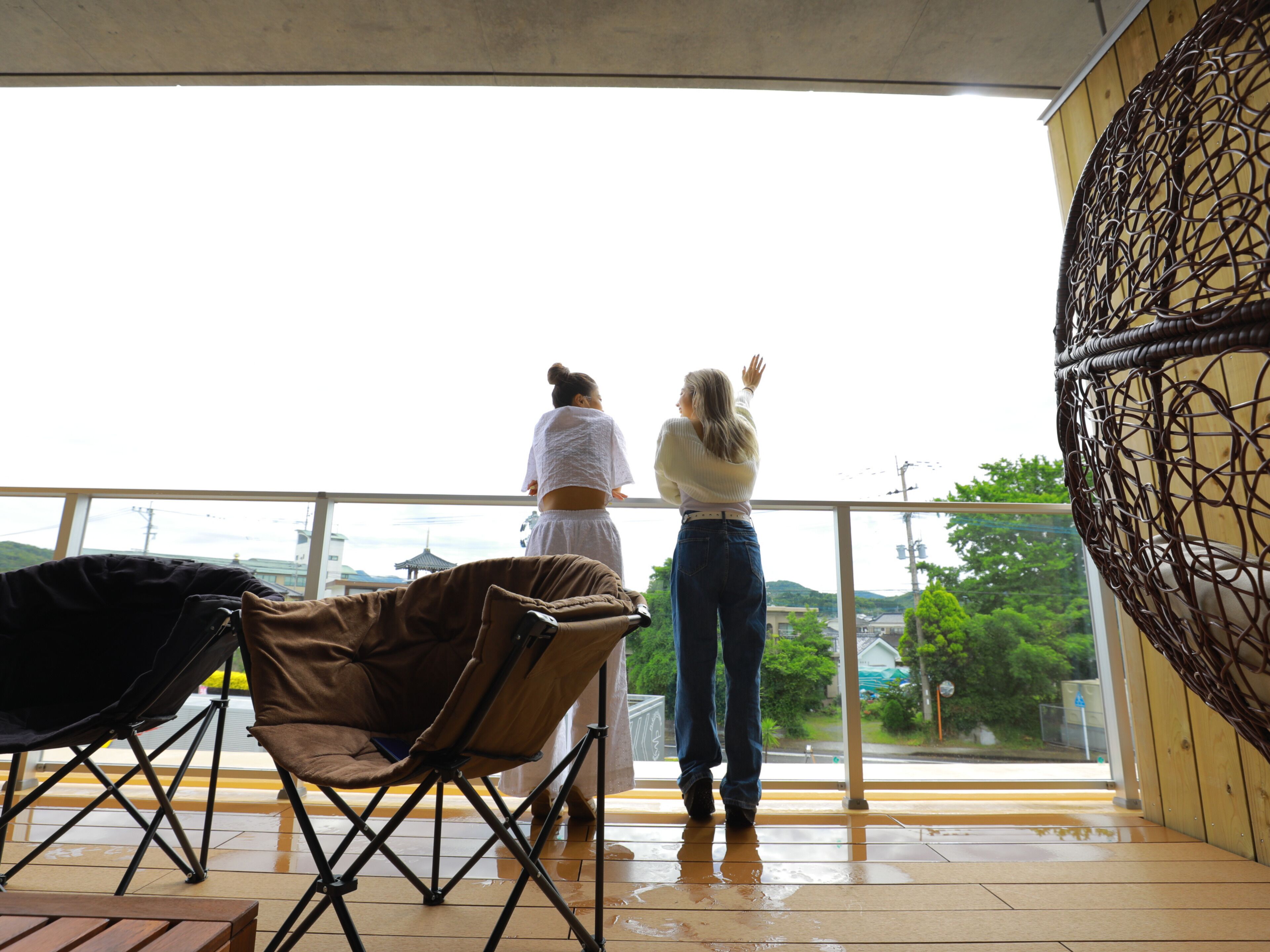 A balcony with a view of a cityscape, a brown folding chair, and a wooden table.