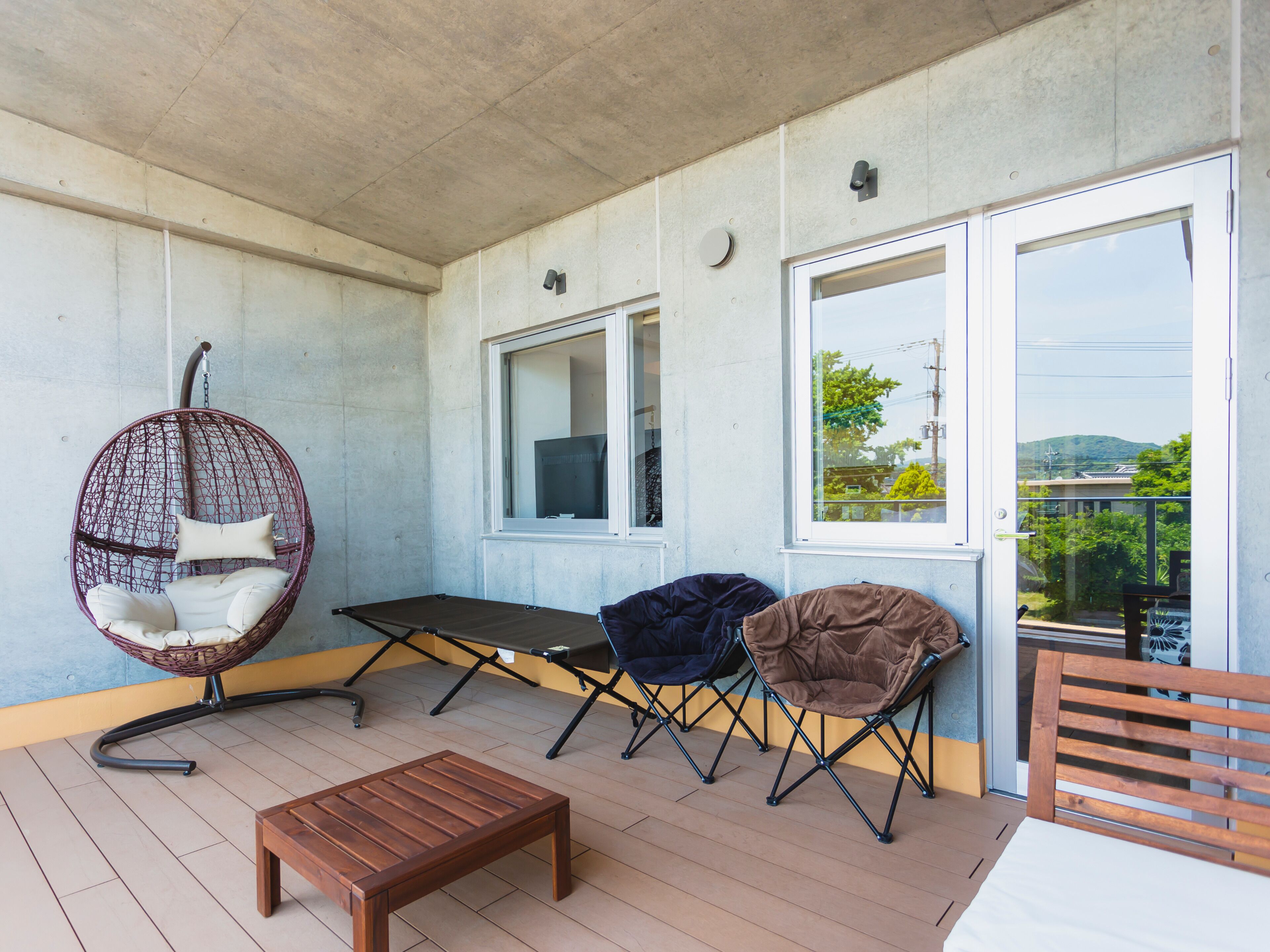 A covered outdoor seating area with a hanging chair, foldable chairs, and a wooden table.