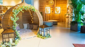 Un coin salon accueillant avec des fauteuils en osier disposés sous une sorte de dôme, une petite table avec une bougie et une grande plante en pot.