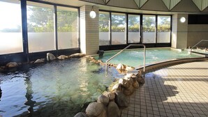 Une piscine intérieure à l’eau claire, entourée de rochers, avec de grandes fenêtres donnant sur l’extérieur.