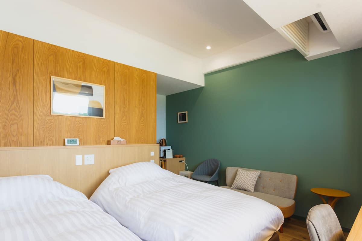 Une chambre d’hôtel avec deux lits, une tête de lit en bois, un mur vert, une petite table et une chaise.