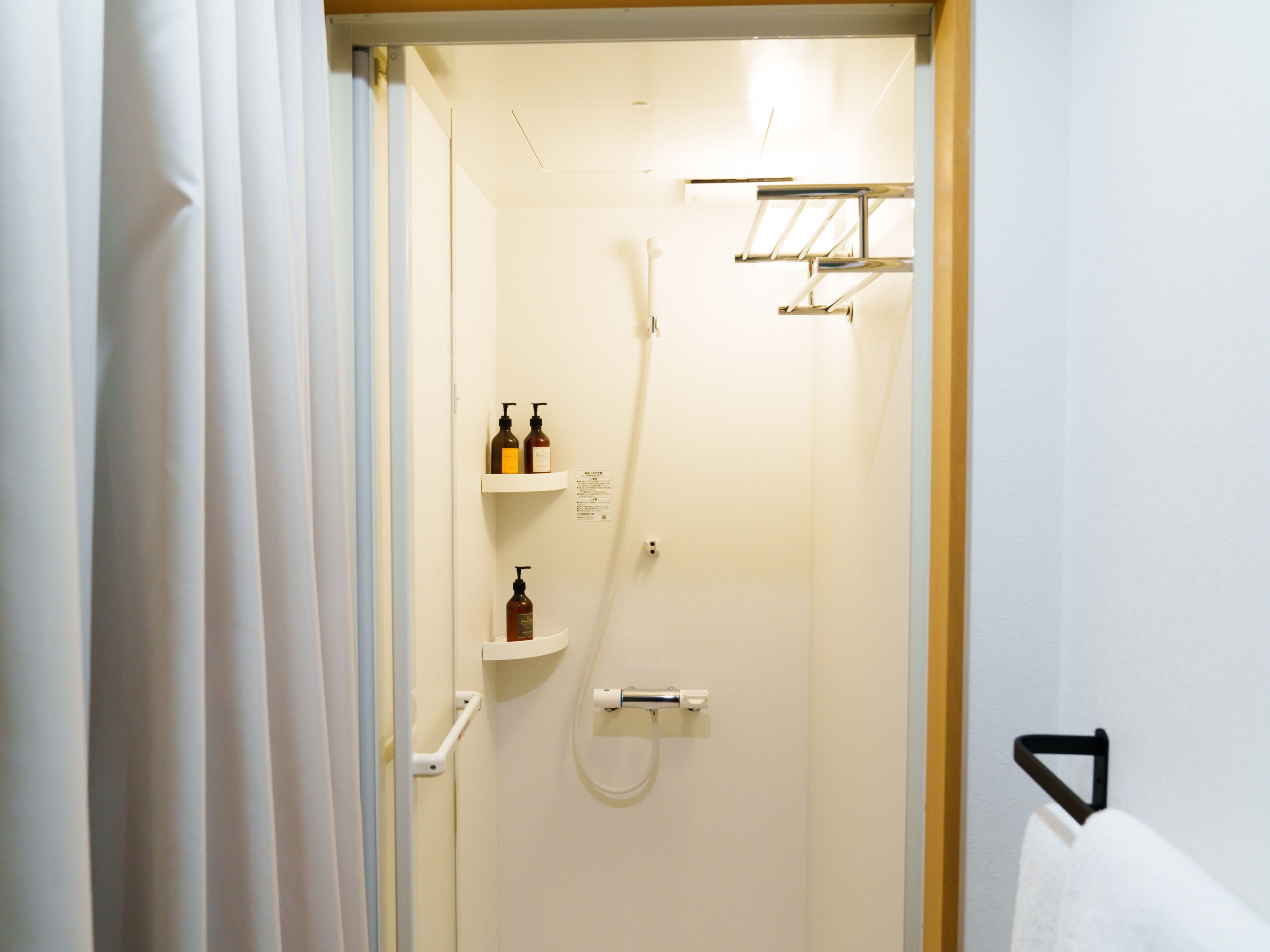Un baño con ducha, un perchero y dos repisas con artículos de tocador.