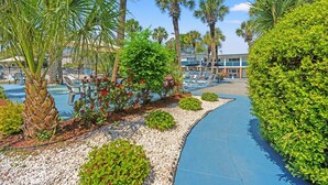 A pool area with palm trees, a pathway, and a building with a pool deck. - Sun Fun Motel (Myrtle Beach)