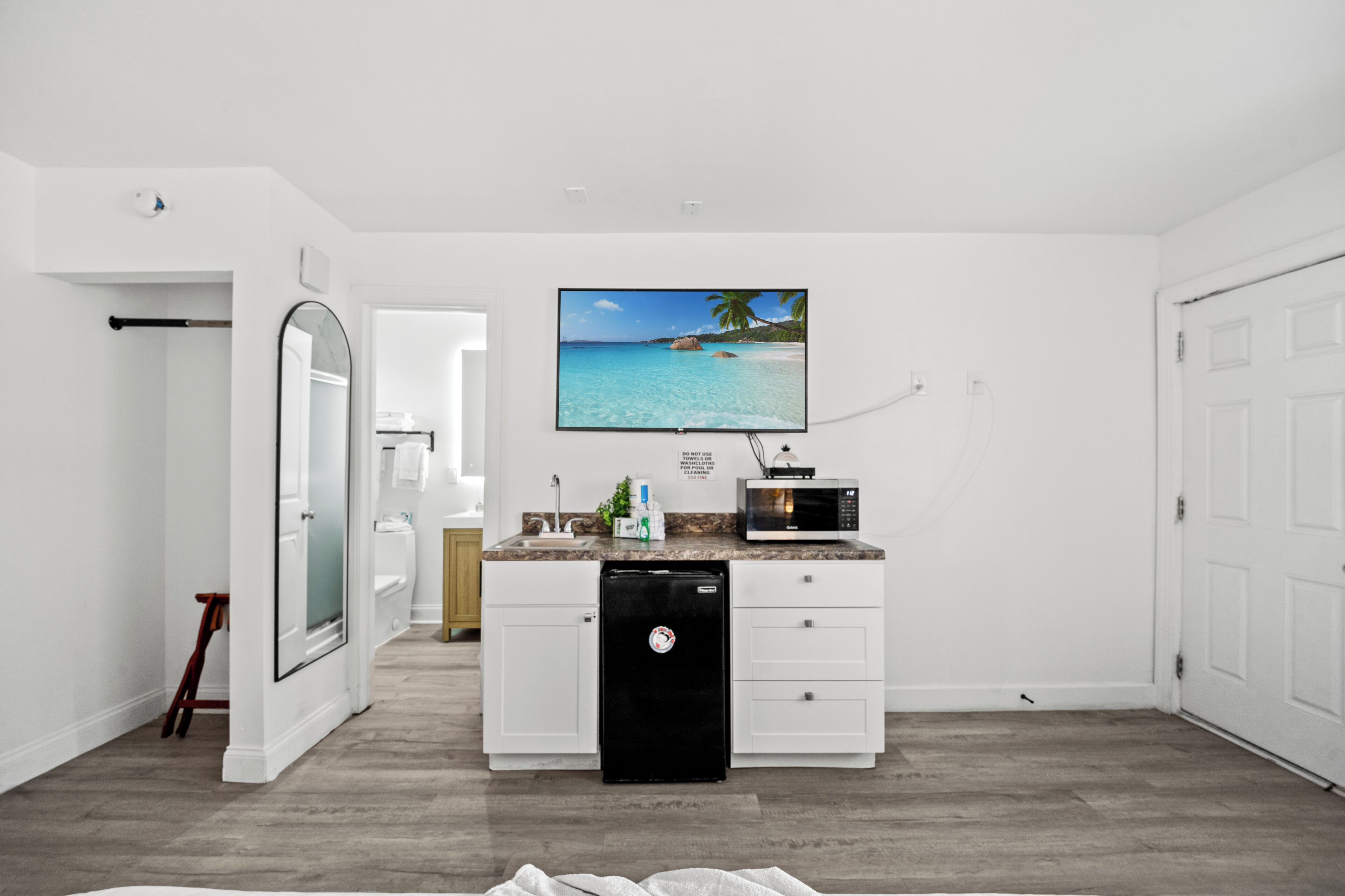 A modern kitchen with a built-in microwave, a refrigerator, and a large flat-screen TV mounted on the wall.