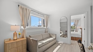 A modern room with a sofa, a wooden side table, a mirror, and a view of the outside. - Sun Fun Motel (Myrtle Beach)