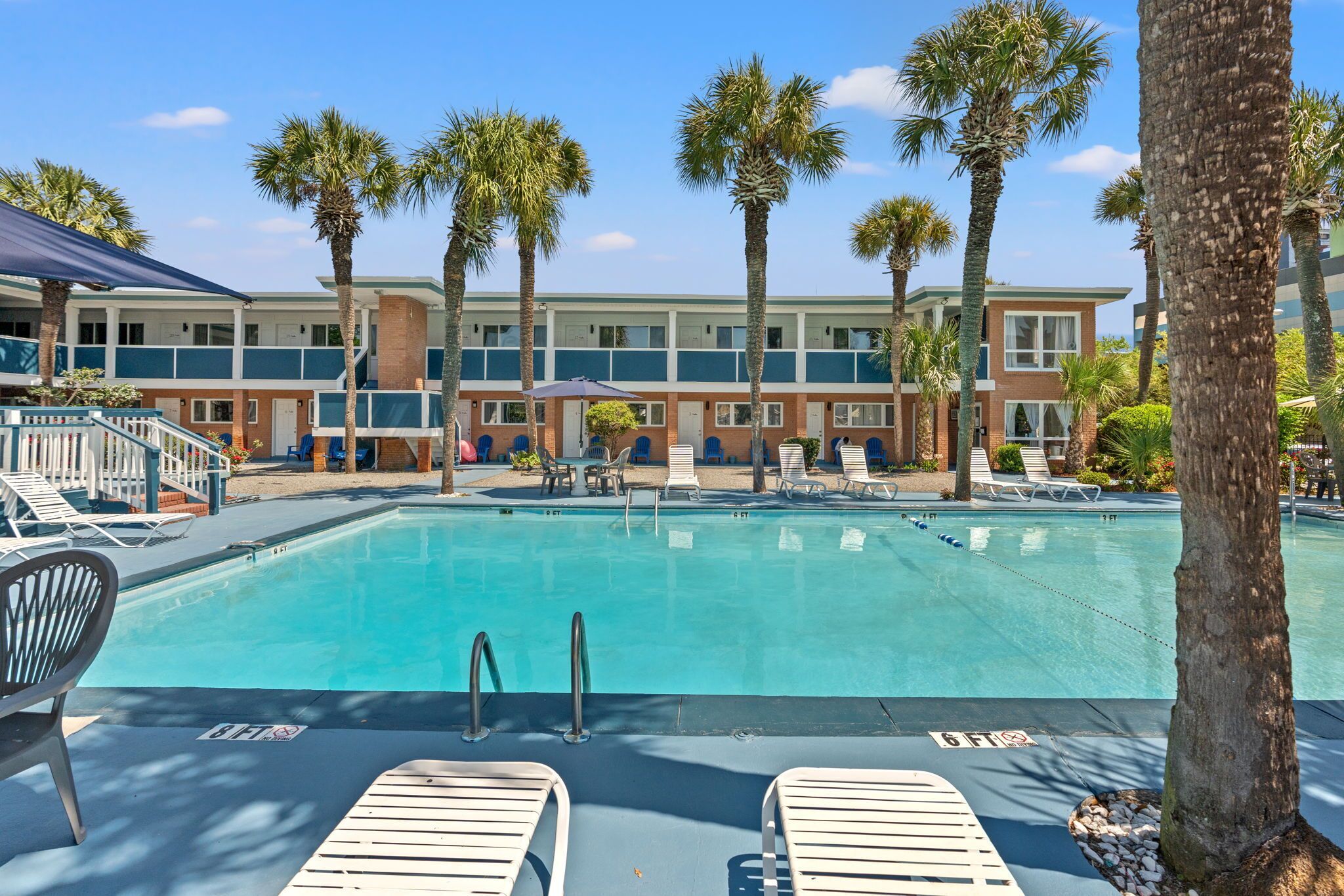 A pool area with lounge chairs, palm trees, and a building with multiple floors and balconies.