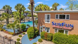 Motel SunFun Boutique con piscina, rodeado de palmeras y un edificio de ladrillo.