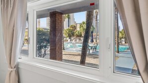 A window with a view of a pool area, including lounge chairs and palm trees. - Sun Fun Motel (Myrtle Beach)