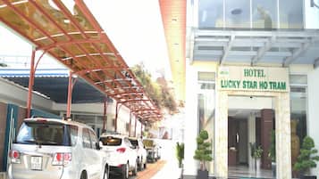 Entrada de hotel com área de estacionamento coberta e vários carros estacionados.