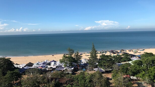 Une plage avec des tentes et des bateaux, des arbres et un ciel dégagé.
