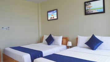 A hotel room with two beds, each with white linens and blue accents, a wooden headboard, and a beach-themed painting on the wall.