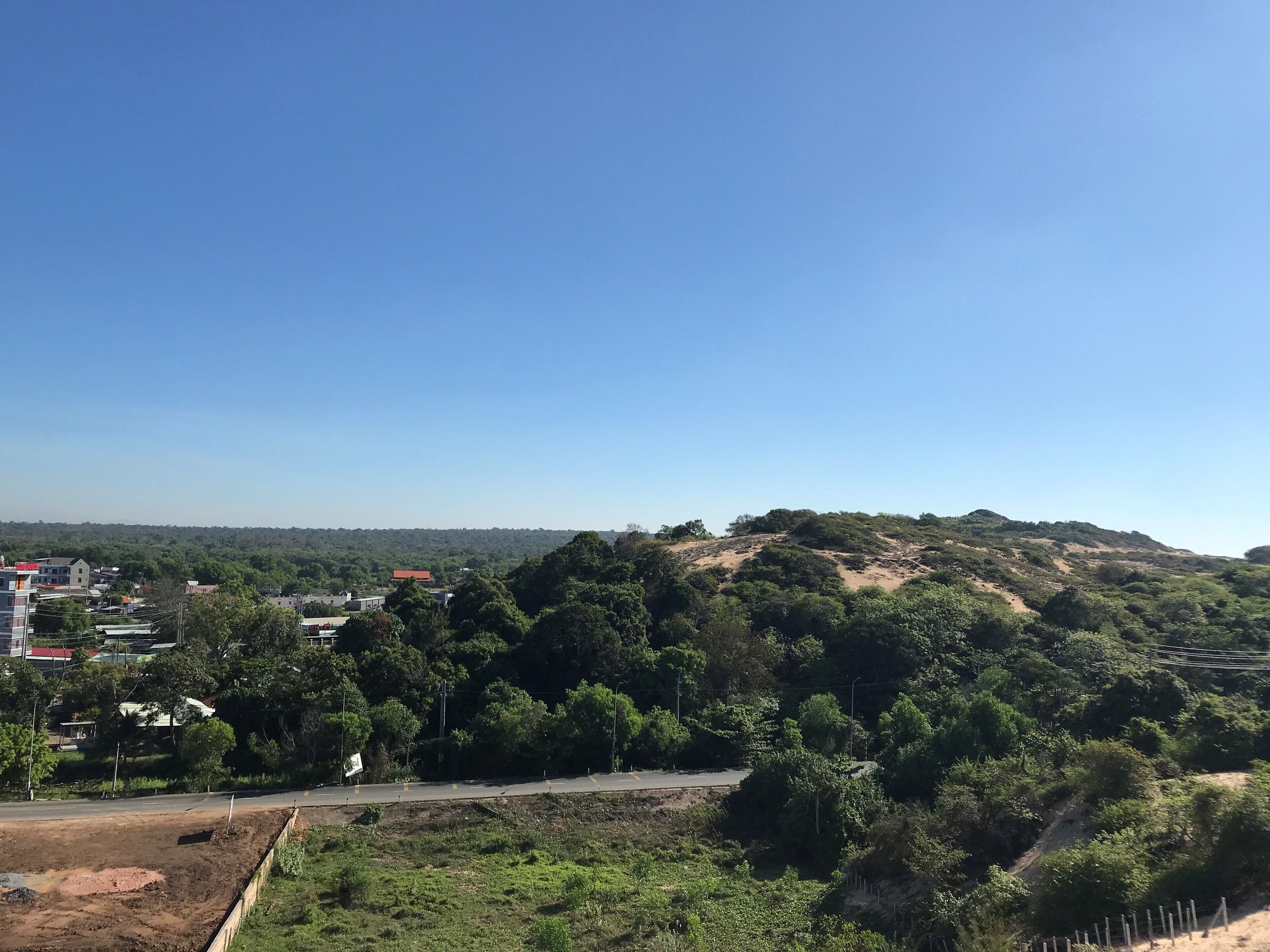 A hilly landscape with a road, buildings, and greenery.