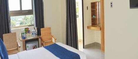 A hotel room with two beds, a desk with a chair, a small kitchenette, and a window with curtains.