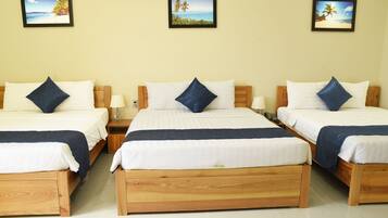 A hotel room with three wooden beds, each with white bedding and blue pillows, and framed tropical beach pictures on the wall.