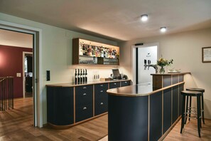 Una cucina moderna con angolo bar, caratterizzata da una dispensa per vini integrata, sgabelli da bar e un piano di lavoro con lavello.