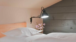 A neatly made bed with white linens, a wall-mounted lamp, and a small vase with pink flowers. - Triple room - Gasthof Rössle (Innerbraz)
