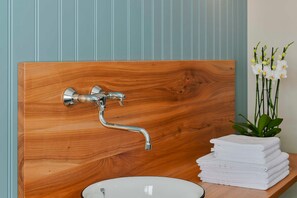 A bathroom with a wooden vanity, a white sink, and a stack of white towels. - Single Room - Gasthof Rössle (Innerbraz)